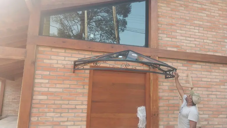 Marquise de vidro com estrutura metálica sobre porta de entrada em fachada de tijolo