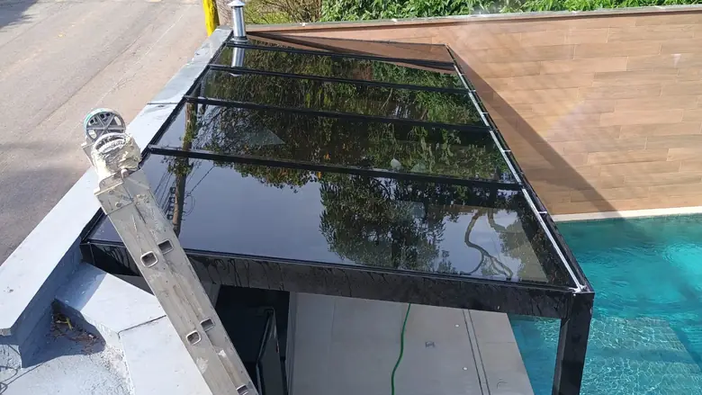 Cobertura de vidro fumê com estrutura metálica ao lado de piscina