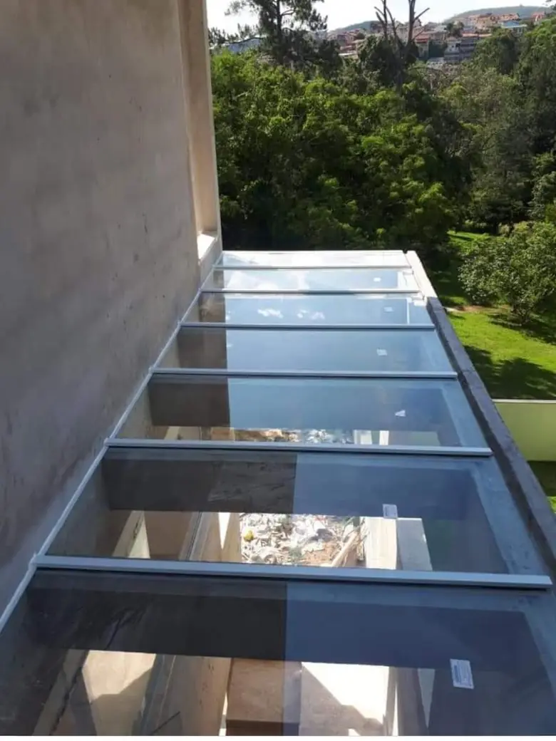 Cobertura de vidro temperado em corredor externo com vista para área verde